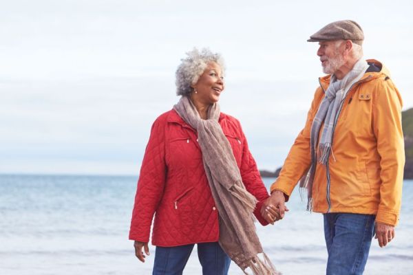 Mixed race senior couple walking on beach holding hands, smiling at one another