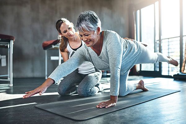 physiotherapist with a patient on a yoga mat exercising with cancer